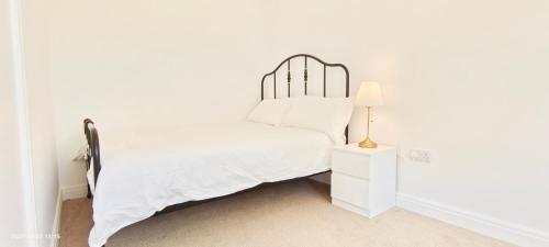 a white bedroom with a bed and a lamp on a nightstand at Phlox Garden in Sutton