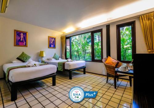 a room with two beds and chairs and windows at Baan Amphawa Resort & Spa - SHA Certified in Amphawa