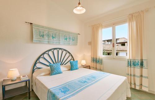 a bedroom with a bed with blue pillows and a window at Residence Le Bouganville in Villasimius