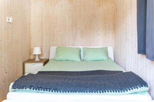 a bed with a blue blanket and two green pillows at Domki Aqua Holiday in Pobierowo