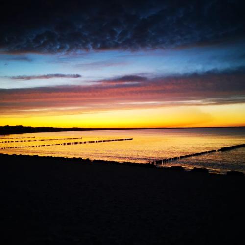 a sunset on the beach with a pier in the water at Albert-INN-Glowe - barrierefrei & 3 Schlafzimmer & Coworking & Strandkorb-saisonal & Sauna im Haus & Fahrräder in Glowe