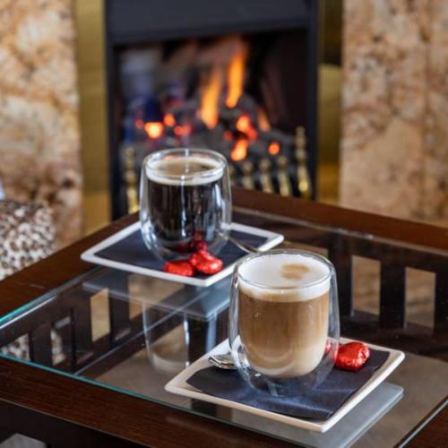 two cups of coffee sitting on a table with a fireplace at Applegarth Villa Hotel & Restaurant (Adult Only) in Windermere