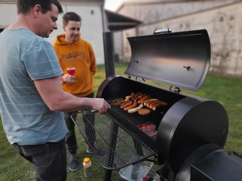 two men are cooking food on a grill at Op 't Roth 12 ruime sfeervolle vakantiewoning in 't groen in Oudenaarde