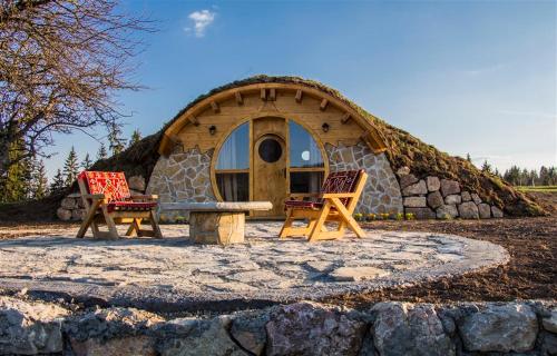 a cabin with two chairs and a table in front of it at Mountain bungalows and a Hobbit House - Jazavčije Rupe in Han Pijesak