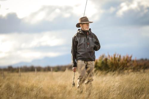 a man in a hat walking through a field at Lago Rosario Lodge in Trevelin