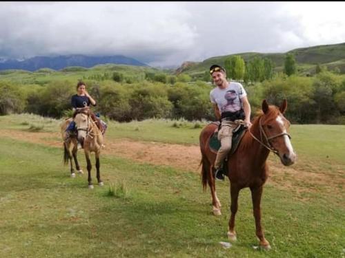 a man and a woman riding horses in a field at Mountain Horse Trekking Guesthouse in Karakol
