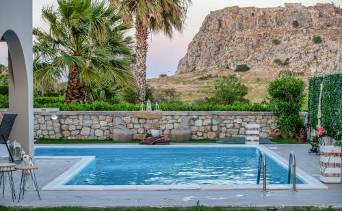 una piscina con una pared de piedra y palmeras en Haraki Villas, en Charaki