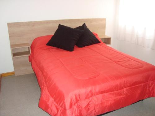uma cama com um edredão vermelho e almofadas pretas em Departamento Andino em Río Cuarto
