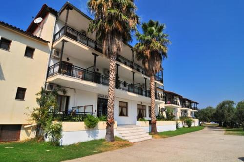 a large white building with palm trees in front of it at Hotel Coral in Skala Rachoniou