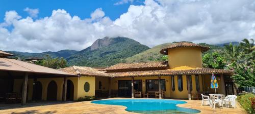 a house with a pool and mountains in the background at Pousada Casa Amarela in Ilhabela
