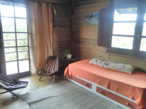 a bedroom with a bed and a chair and windows at Horneritos - Cabaña en Villa Serrana in Villa Serrana