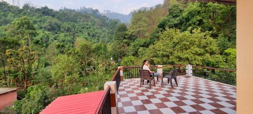 a woman sitting on a balcony looking at the forest at Karthik Resorts, Jeolikote Nainital in Nainital