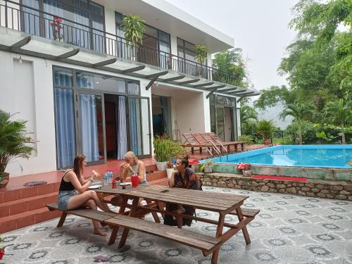 a group of people sitting at a picnic table by a pool at Hugo Homestay in Phong Nha
