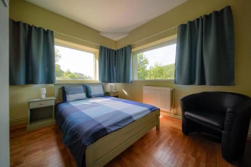 a bedroom with a bed and a chair and two windows at Parkside Vila in Odorheiu Secuiesc