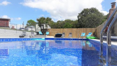 a blue swimming pool with chairs and a fence at Greenways Valley Holiday Park in Great Torrington