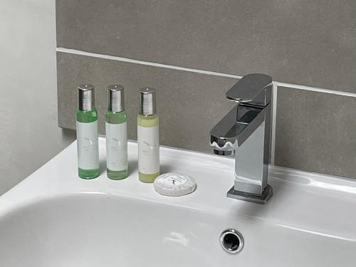 a bathroom sink with three bottles and a faucet at Holiday House at 22, Contemporary 3 bedroom cottage in historic Wigtown in Wigtown