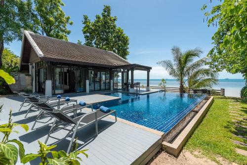 a pool with chairs and a pavilion next to the ocean at Beach Front Villa in Ban Bang Po