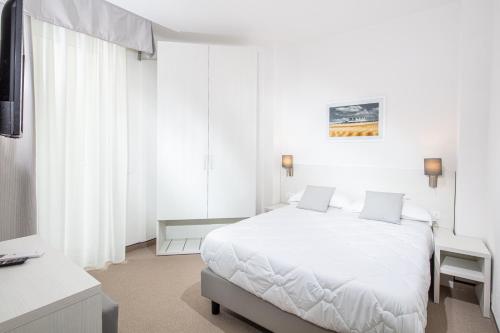 a white bedroom with a white bed and a desk at Hotel Centrale in Lignano Sabbiadoro