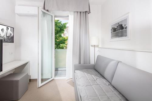 a white bedroom with a couch and a mirror at Hotel Centrale in Lignano Sabbiadoro