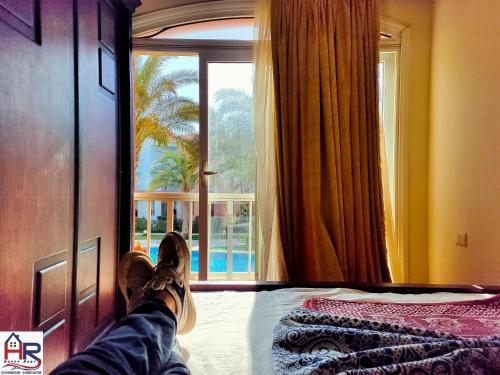 a person with their feet on a bed looking out a window at Chalets in Porto Matrouh Families Only in Marsa Matruh