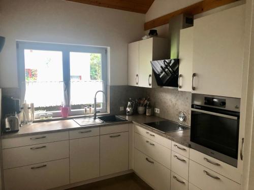 cocina con armarios blancos, fregadero y ventana en Wiehler- Ferienwohnung, en Wiehl