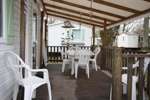 une terrasse couverte en bois avec des chaises blanches et une table dans l'établissement MOBIL-HOME 6 PERSONNES CAMPING EUROLAC BORD LAC AUREILHAN, à Aureilhan