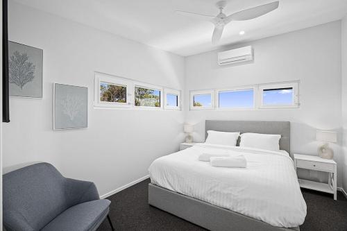 a white bedroom with a bed and a chair at Bluehaven Woolgoolga - Brand New, Ocean Views, 200m Stroll to Beach and Restaurants! in Woolgoolga