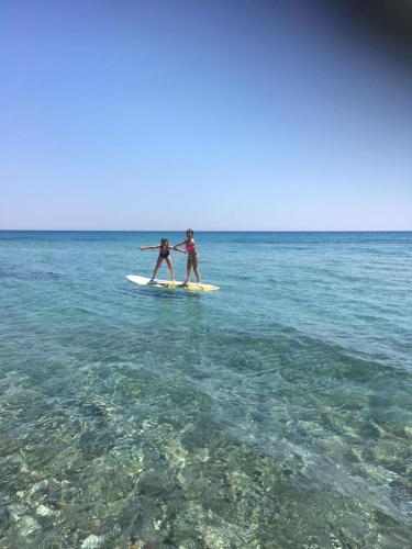 two people standing on a surfboard in the ocean at MOLA PAPAYA STUDIOS in Mola Kalyva