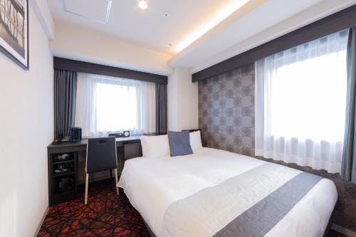 名古屋市にあるホテルアクテル名古屋錦のベッド、デスク、窓が備わるホテルルームです。