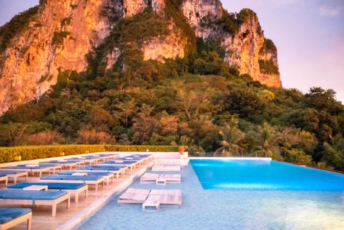 a pool with lounge chairs and a mountain in the background at BlueSotel SMART Krabi Aonang Beach - Adults only in Ao Nang Beach