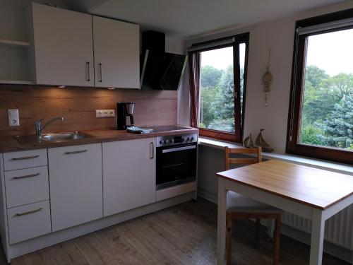 eine Küche mit weißen Schränken, einem Tisch und Fenstern in der Unterkunft Doris` Hus in Travemünde
