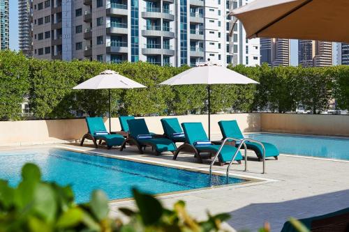 un grupo de sillas y sombrillas junto a una piscina en Radisson Blu Residence, Dubai Marina, en Dubái