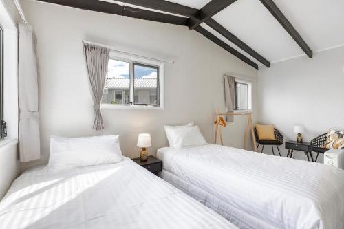 two beds in a room with white walls and windows at Couches, Bar Table & Kawau View in Snells Beach
