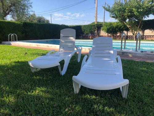 two white lounge chairs sitting in the grass near a pool at Chalet con piscina privada en Vinaròs in Vinarós