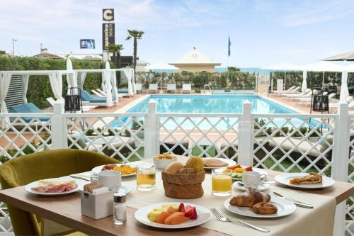 a table with breakfast food on a balcony with a pool at Hotel Delle Rose in Lido di Jesolo