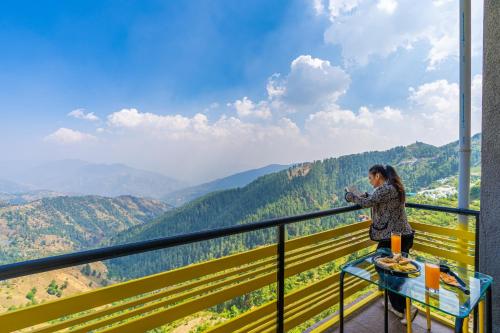 a woman taking a picture of the mountains from a balcony at The Hosteller Kufri, Shimla in Kūfrī