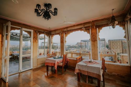 a dining room with tables and chairs and windows at The Gulaal in Jaisalmer