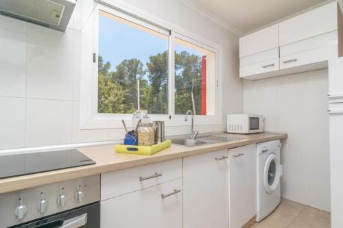 a white kitchen with a sink and a window at Es Pins in Font de Sa Cala