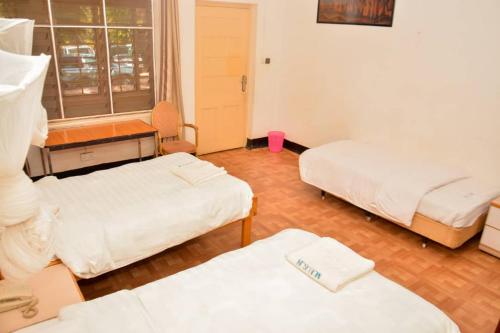 a room with three beds and a desk and window at MAKERERE UNIVERSITY GUEST HOUSE in Kampala