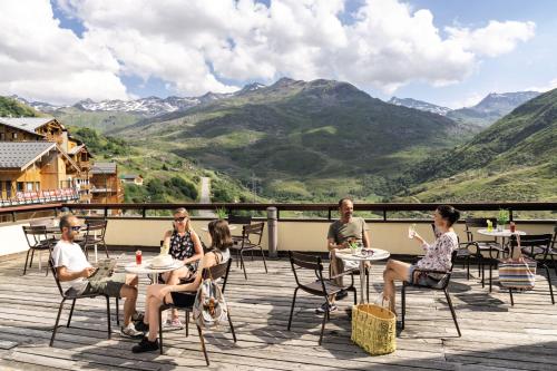 a group of people sitting at tables on a deck with mountains at Hôtel Les Menuires Les Bruyères in Les Menuires