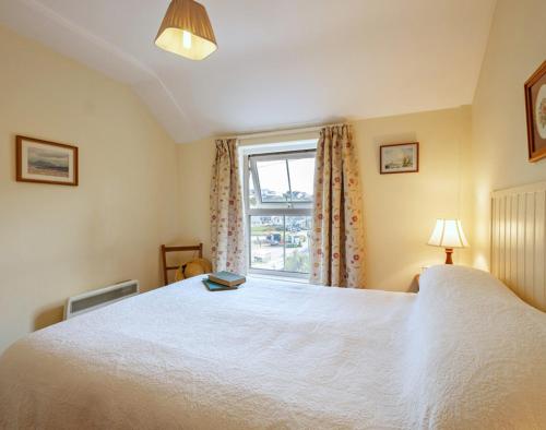 a bedroom with a large white bed and a window at Coppingers Cottage in Polzeath
