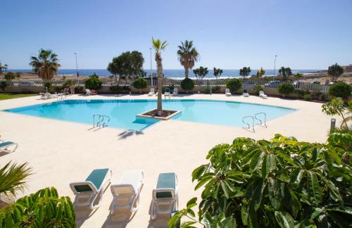 a swimming pool with lounge chairs and the beach at MEDANO4YOU Scotts Place in El Médano