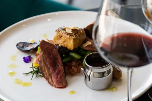 a white plate with food and a glass of wine at Allure Healthy Hotel & Spa in Eger
