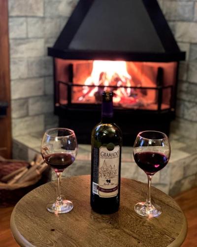 two glasses of wine sitting on a table in front of a fireplace at Chalé Temático em Pipa de Vinho - Parada da Pipa Chalés in Canela