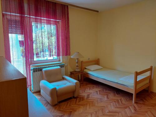 a bedroom with a bed and a chair and a window at Hills Apartment in Niš