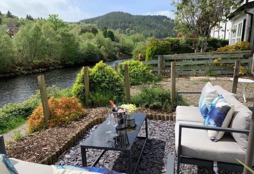 a patio with a couch and a table next to a river at Coorie Doon in Cairnbaan