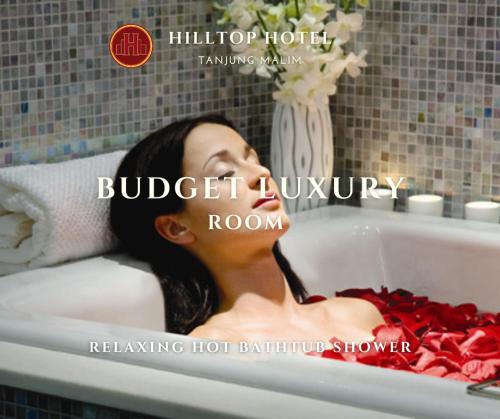 a woman laying in a bath tub with red towels at Hilltop Hotel Tanjung Malim in Tanjung Malim