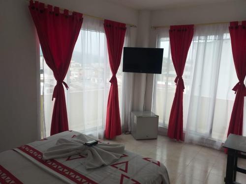 Schlafzimmer mit roten Vorhängen und einem Bett mit einem TV in der Unterkunft Hotel Luis Ángel in Mocoa