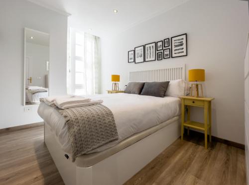 a white bedroom with a large bed and a yellow table at Precioso piso nuevo dentro del recinto amurallado in Lugo