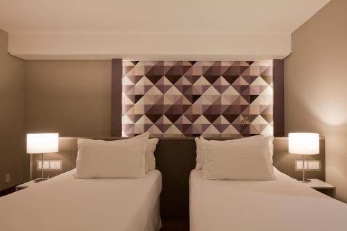 two beds in a hotel room with two lamps at NH Collection Curitiba in Curitiba
